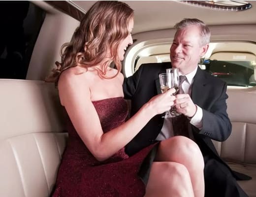 A young woman is drinking champagne with an older man in a luxury car